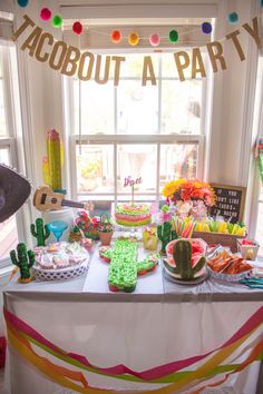 a table topped with lots of cake and desserts next to a window filled with balloons