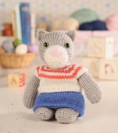 a knitted gray cat sitting on top of a white table next to books and toys