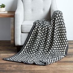 a white chair with a black and white blanket on it next to a wooden table