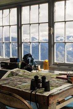 a table with binoculars and other items on it in front of large windows overlooking mountains