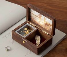 an open wooden box with two rings in it on top of a table next to a book