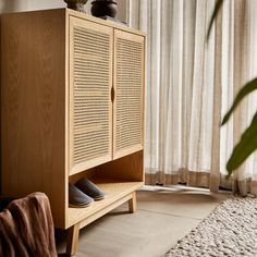 a wooden cabinet sitting in front of a window next to a rug and potted plant