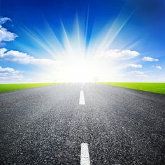 an empty road with the sun shining down on it and green grass in the background