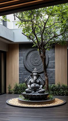 a buddha statue sitting on top of a wooden floor next to a tree in front of a building