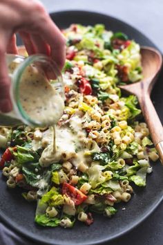 a person pouring dressing into a salad on a black plate with wooden utensils