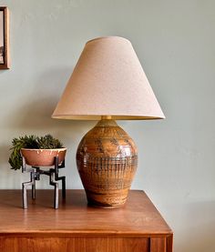 a lamp sitting on top of a wooden table next to a vase and potted plant