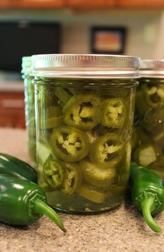 green peppers are in a glass jar on the counter next to some pepper slices and jalapenos