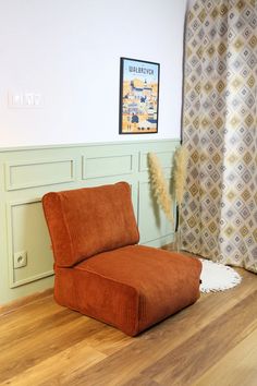 an orange chair sitting on top of a hard wood floor next to a window with curtains