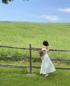 a woman in a white dress is standing near a fence and holding a bouquet of flowers