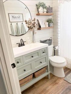 a white toilet sitting next to a bathroom sink under a mirror on top of a wooden floor