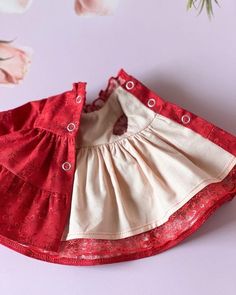 a red and white dress with buttons on the collar is sitting on a table next to pink flowers