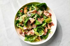 a white bowl filled with lettuce and chicken salad on top of a table