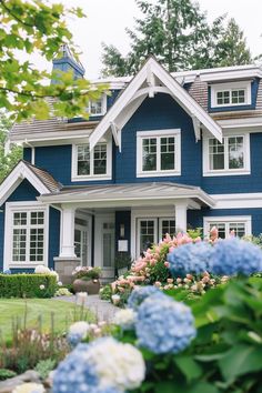 a blue house with white trim and lots of flowers in front of the windows on each side