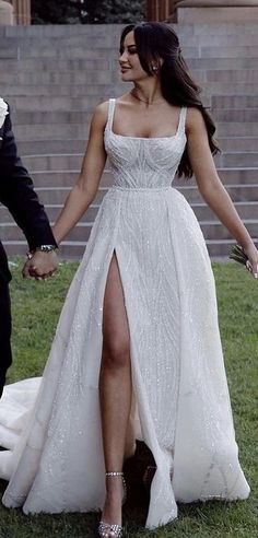 a man and woman in formal wear holding hands while walking on grass with stairs behind them