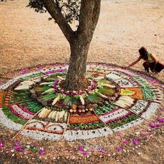 a woman kneeling down next to a tree in the middle of a field with flowers on it