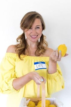 a woman in yellow is holding some lemons and a bag with the word life on it