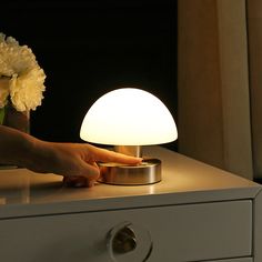 a person's hand on a table next to a lamp with flowers in it