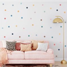 a pink couch sitting in front of a wall with polka dot decals on it