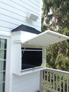 an open window on the side of a white house with trees in the back ground