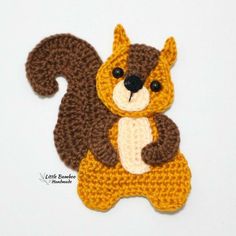 a crocheted squirrel brooch sits on its hind legs and holds it's tail