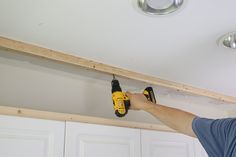 a man is holding a drill in his right hand and drilling the ceiling with a screwdriver