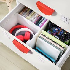 an organized drawer with headphones, books and magazines in it on a wooden floor