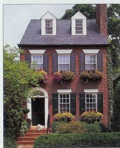 a large brick house with two story windows and shutters on the front, surrounded by greenery