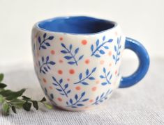 a blue and white coffee cup sitting on top of a table next to a plant