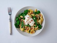 a white plate topped with pasta and broccoli next to a knife and fork