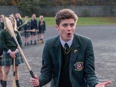 a young man in a green jacket holding a baseball bat and wearing a school uniform