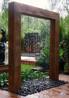 an outdoor fountain in the middle of a wooden deck with rocks and plants around it