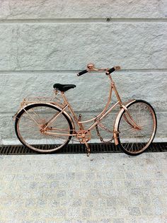 a gold colored bike parked on the sidewalk next to a building with a grate in front of it