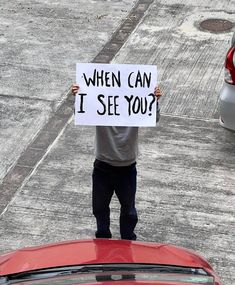 a man holding up a sign that says when can i see you?