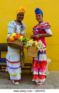 two women dressed in colorful clothing standing next to each other with baskets full of flowers