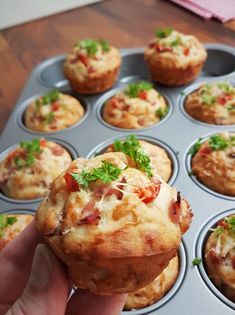 a person holding up a muffin in a cupcake tin with other muffins