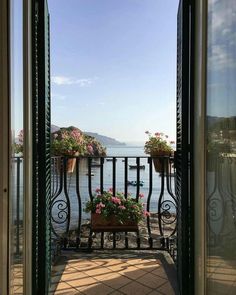 an open door leading to a balcony with potted plants on it and the ocean in the background