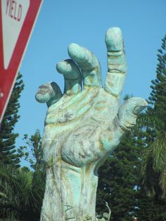 there is a large hand statue in front of a stop sign with trees behind it