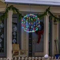 a christmas ball hanging from the side of a house with wreaths and lights on it