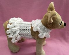 a stuffed dog wearing a white crochet dress on top of a pink background