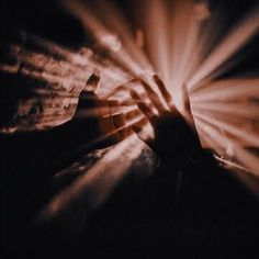 a person holding their hand out in front of the light coming from behind them on a dark background