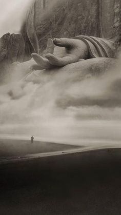 a black and white photo of a person standing in front of a large statue on the side of a mountain