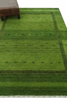 a green area rug with a brown leather bench on the ground and an ottoman in front