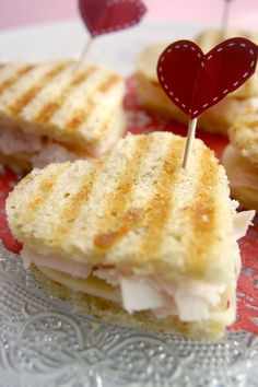 small sandwiches with toothpicks in the shape of a heart on a glass plate