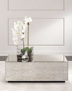 a glass vase with flowers in it sitting on a silver table next to a white wall