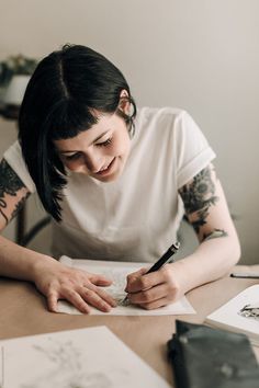 a woman sitting at a table writing with a pen and paper in front of her