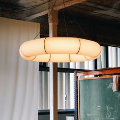 a light hanging from the ceiling over a chalkboard in a room with white curtains