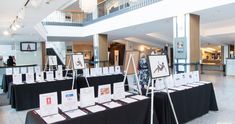 several tables with black tablecloths and pictures on them in a large room filled with people