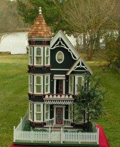 a doll house on top of a red table cloth in front of some trees and water