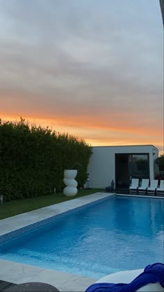 an empty swimming pool with lounge chairs around it and the sun setting in the background