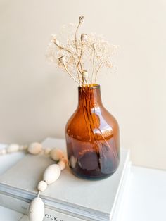 a brown vase sitting on top of a book next to a white beaded necklace